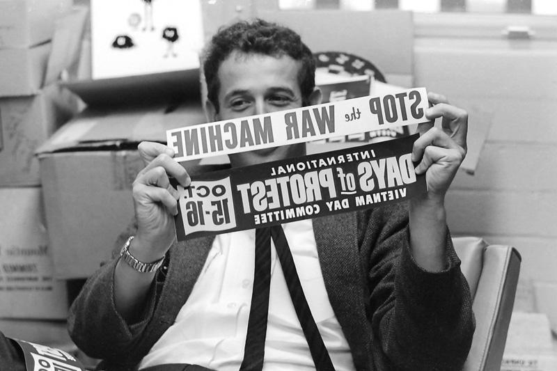 爱德华·桑普森, 社会心理学副教授, 拿着两个保险杠贴纸:“国际抗议越南日委员会”, Oct. 15-16”和“停止战争机器.1965年9月16日，摄于他的办公室.